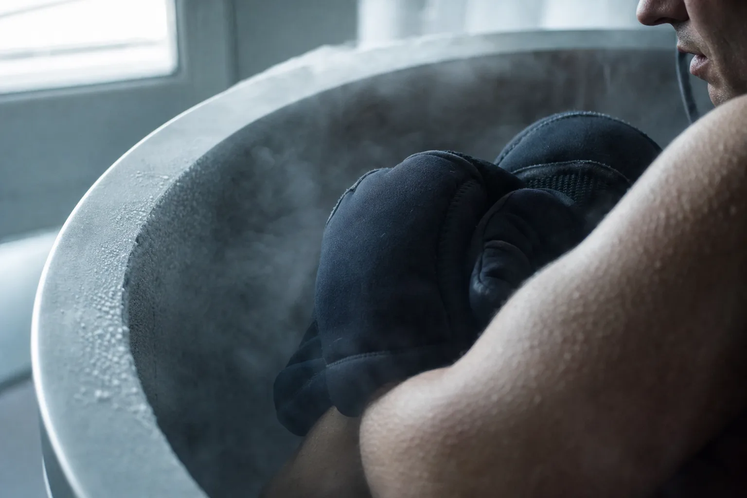 Mains protégées par des gants isolants dans une cabine de cryothérapie givrée, entourées de vapeur froide